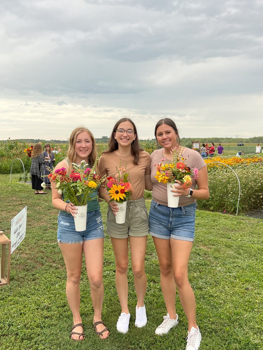 Three young female adults each holding their containers of flowers at a You-Pick event.
