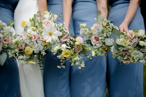 Bridesmaids in blue satin dresses and the bride. All are holding Fleurish Flower Farm bouquets.