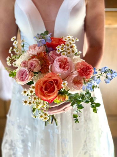 A bride holding a flower bouquet in hues of pinks and oranges.