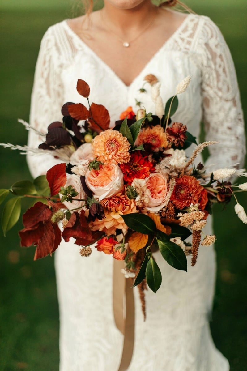 A bride holding a Fleurish Flower Farm bouquet in hues of reds and oranges.