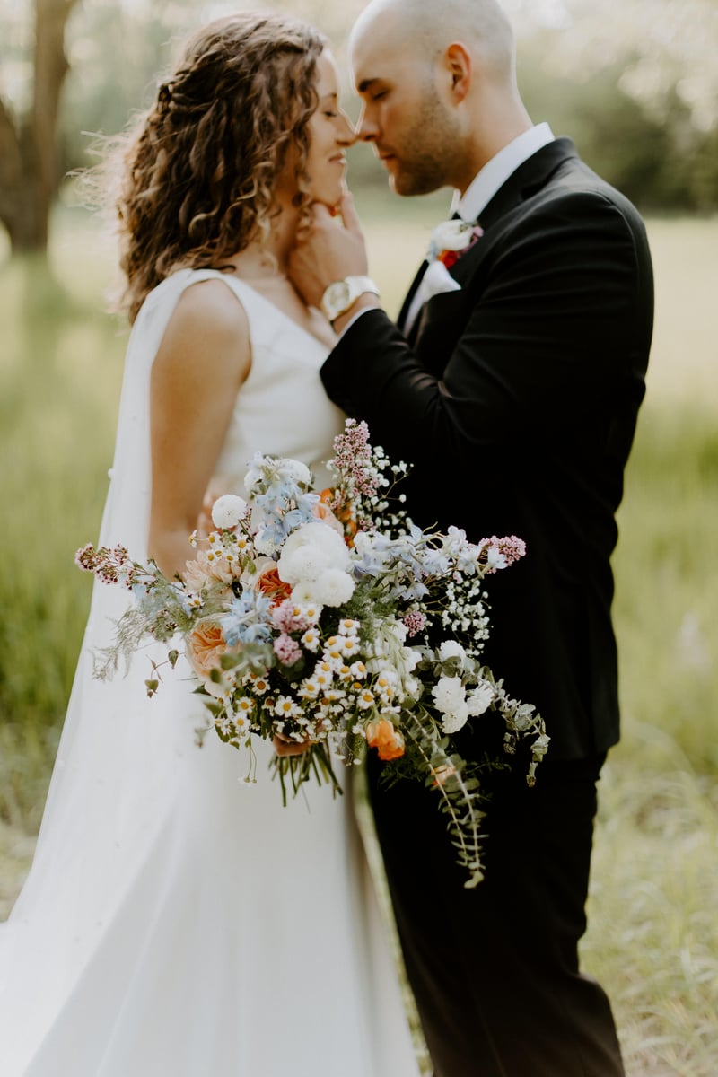 A bride and groom share an intimate moment, the bride is holding a large flower bouquet from Fleurish Flower Farm.