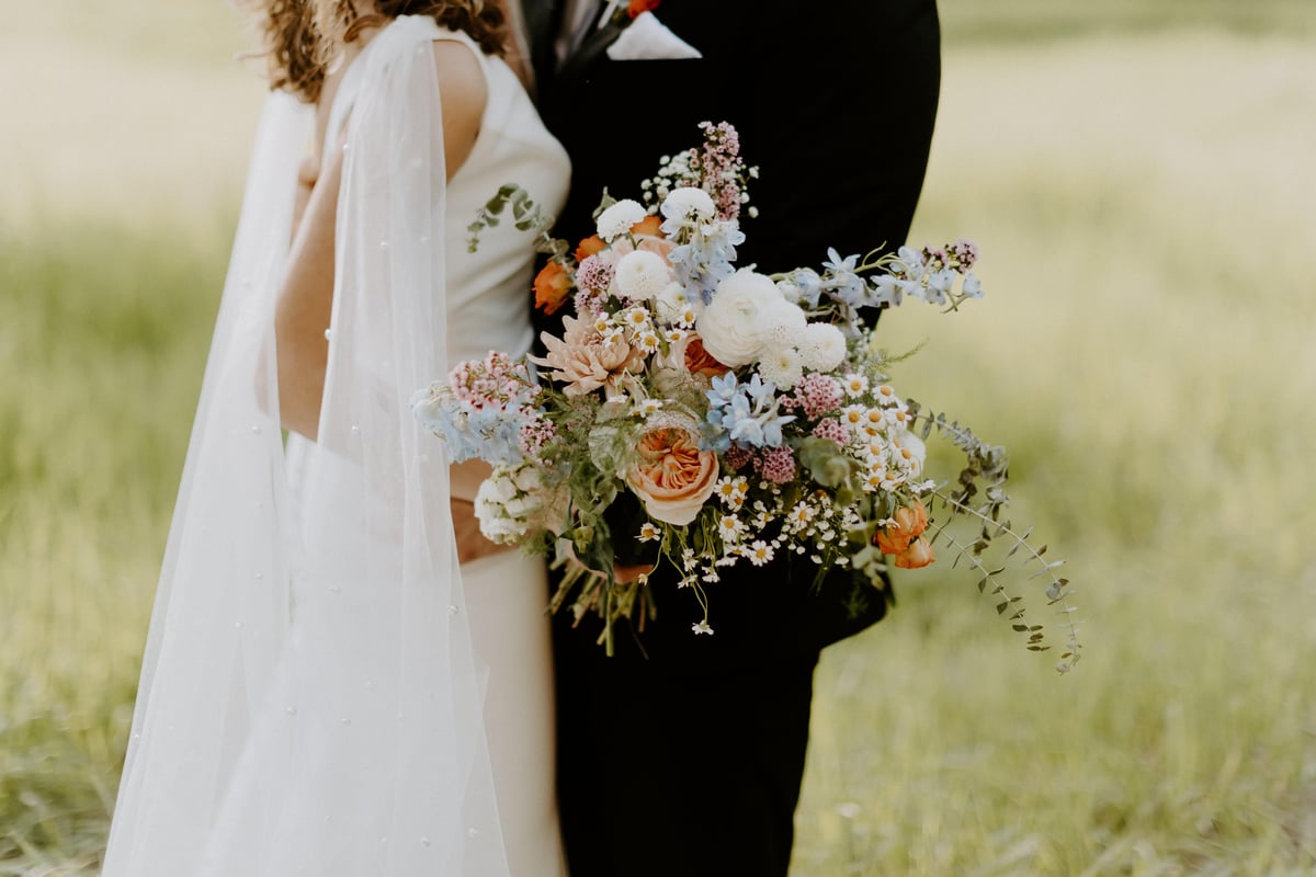 Bride and groom embracing. The bride is holding a Fleurish Flower Farm bouquet.